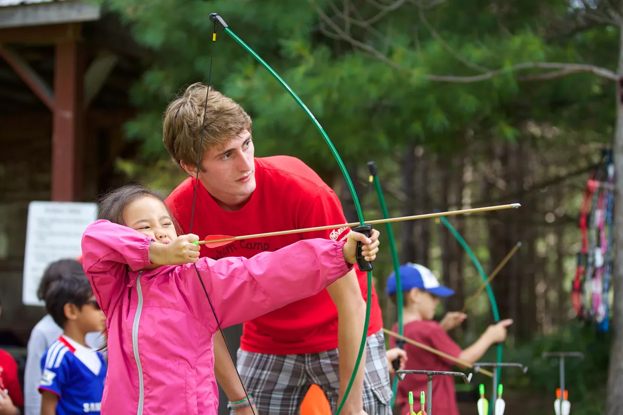 Camper and camp councilor aiming an arrow.